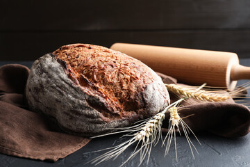 Loaf of fresh bread, rolling pin and spikes on black table, closeup