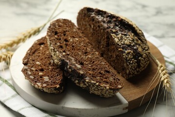 Pieces of fresh rye bread with seeds and spikes on white marble table, closeup