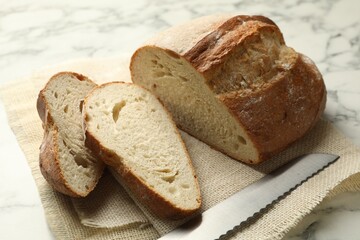 Pieces of fresh bread and knife on white marble table, closeup
