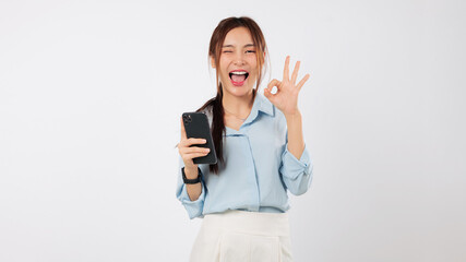 Happy excited young Asian woman holding a mobile phone, showing an ok gesture sign. She is thrilled...