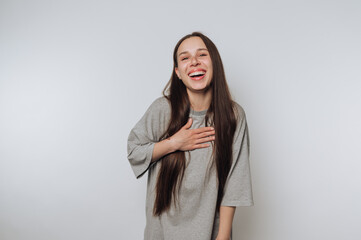 A young woman with long hair laughing and holding her chest, wearing a gray shirt.