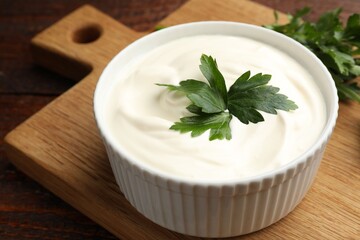 Tasty sour cream with parsley on wooden table, closeup