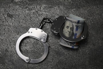 Corruption. Handcuffs and dollar bills on grey table, top view