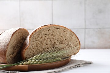 Pieces of fresh bread and green wheat spikes on white wooden table, closeup