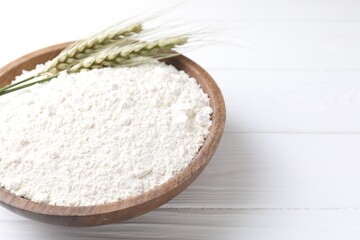 Flour and green wheat spikes in bowl on white wooden table, closeup. Space for text