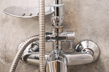 Shiny metal shower faucet closeup. Bathroom plumbing fixture with hose. Modern wall-mounted water...