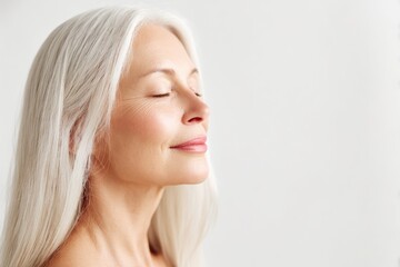 A senior Caucasian woman with long white hair and closed eyes. She has a serene expression, set against a plain white background. The focus is on tranquility and beauty.