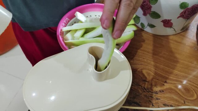 Someone placing slices of fresh bottle gourd or calabash gourd into a juicer to prepare a healthy drink at home.