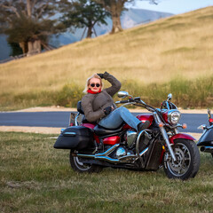 Confident blonde woman relaxing on a red cruiser motorcycle, posing stylishly on a countryside road...