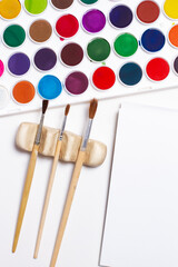 Paintbrushes and watercolor paints on a white background in a top view