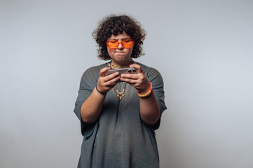 Person with curly hair wearing orange sunglasses, focused on a smartphone.