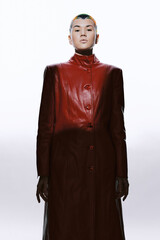 Woman in a long red leather coat stands confidently against a bright white background, showcasing...