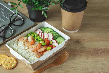 lunch break.Rice with shrimps and vegetables in paper take away box on desk