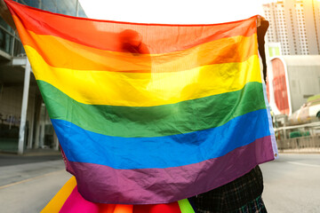 Female couple are holding a rainbow flag high in the air,a symbol of lgbtq pride,while posing outdoors.