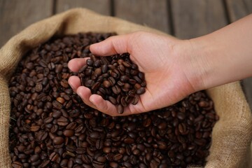 A hand scoops a handful of fresh, raw coffee beans from a burlap sack