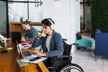 Latin young man in wheelchair working at office in Mexico Latin America, hispanic coworkers and business teamwork in concept of disability and disabled person