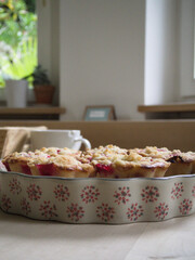 Close-up of berry muffin on vintage floral plate with warm light and rustic tea mug behind.