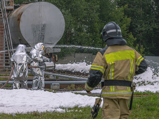 Firefighters in protective clothing use a foam generator to supply foam to extinguish the fire....