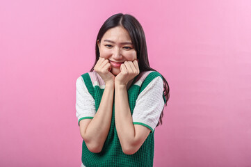 Asian woman with a playful expression poses with clenched fists under her chin, wearing a green...