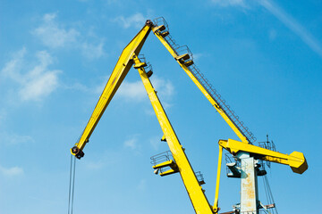 Low angle view of a bright yellow port crane with ladders and pulleys, set against a clear blue sky. Ideal for illustrating global shipping, heavy industry, logistics, port operations, and maritime