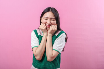 Asian woman with a playful expression poses with clenched fists under her chin, wearing a green...