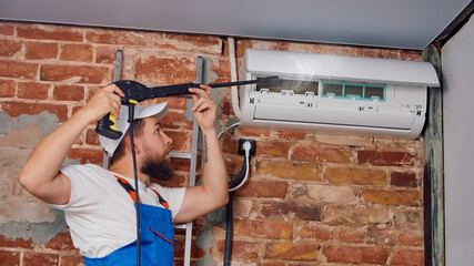 Technician with drill installing wall-mounted air conditioner on brick wall. Concept of fixing HVAC...