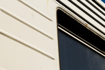 Close-up view of a train car side wall with a rectangular window and ribbed metal surface. The frame shows signs of weathering and rust, highlighting industrial aesthetics and transportation design
