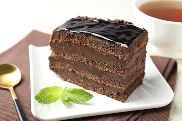 Piece of chocolate cake served with mint and spoon on table, closeup