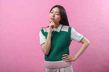 Asian woman in a green sweater posing with a thinking gesture, resting her chin on her hand while...