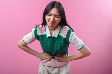 Asian woman clutching her stomach with a pained facial expression, suggesting abdominal discomfort...