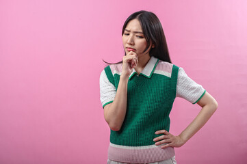 Asian woman in a green sweater posing with a thinking gesture, resting her chin on her hand while...