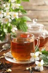 Aromatic jasmine tea in glass cup, teapot, brew and flowers on wooden table, closeup