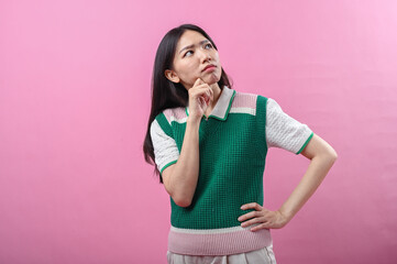Asian woman in a green sweater posing with a thinking gesture, resting her chin on her hand while...