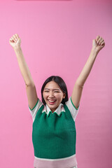 Asian woman celebrating with both arms raised in triumph, smiling brightly in a green sweater and...
