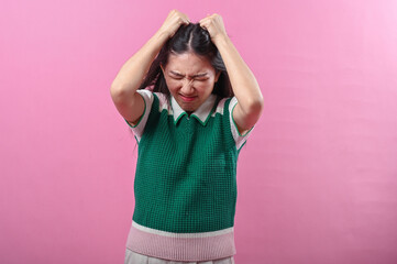 Asian woman pulling her hair in frustration and closing her eyes tightly, expressing extreme stress...