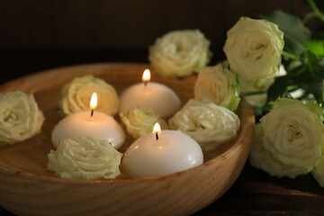 Burning candles, water and rose flowers in bowl on wooden table, closeup