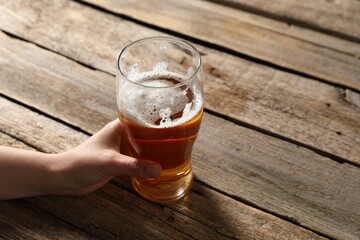 Woman with glass of beer at wooden table, closeup. Space for text