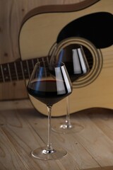 Acoustic guitar and glasses of red wine on wooden table