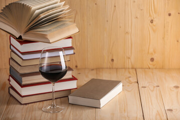 Glass of red wine and stacked books on wooden table. Space for text