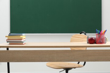 Different school stationery and red apple on wooden table near blackboard indoors