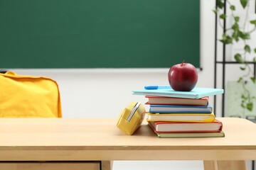 Different school stationery and red apple on wooden table near blackboard, space for text