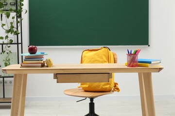 Different school stationery and red apple on wooden table near blackboard indoors