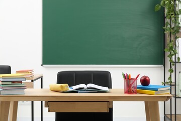 Different school stationery and red apple on wooden table near blackboard indoors