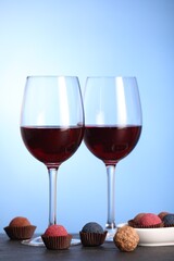 Delicious truffle bonbons and wine on black table against blue background