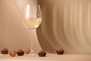 Delicious truffle bonbons and wine on beige background. Space for text