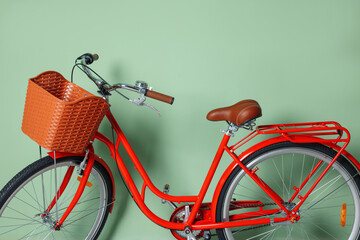 Red bicycle with basket near light green wall indoors, closeup