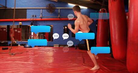 Standing shirtless martial artist in black shorts facing punching bags in dojo, copy space