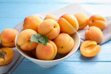 Fresh apricots with green leaves on light blue wooden table, closeup