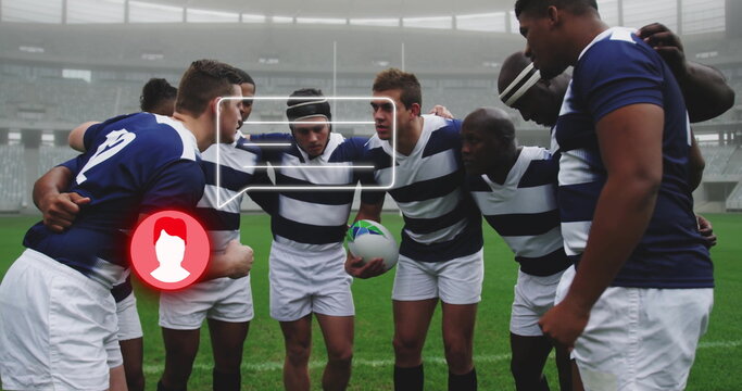 Eight rugby players huddling in jerseys on grass in covered stadium, with green white rugby ball