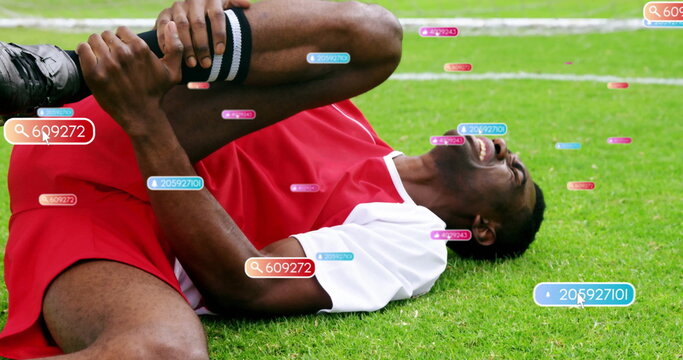 Clutching right knee while lying on grass field wearing red jersey, striped socks and digital tags - Powered by Adobe